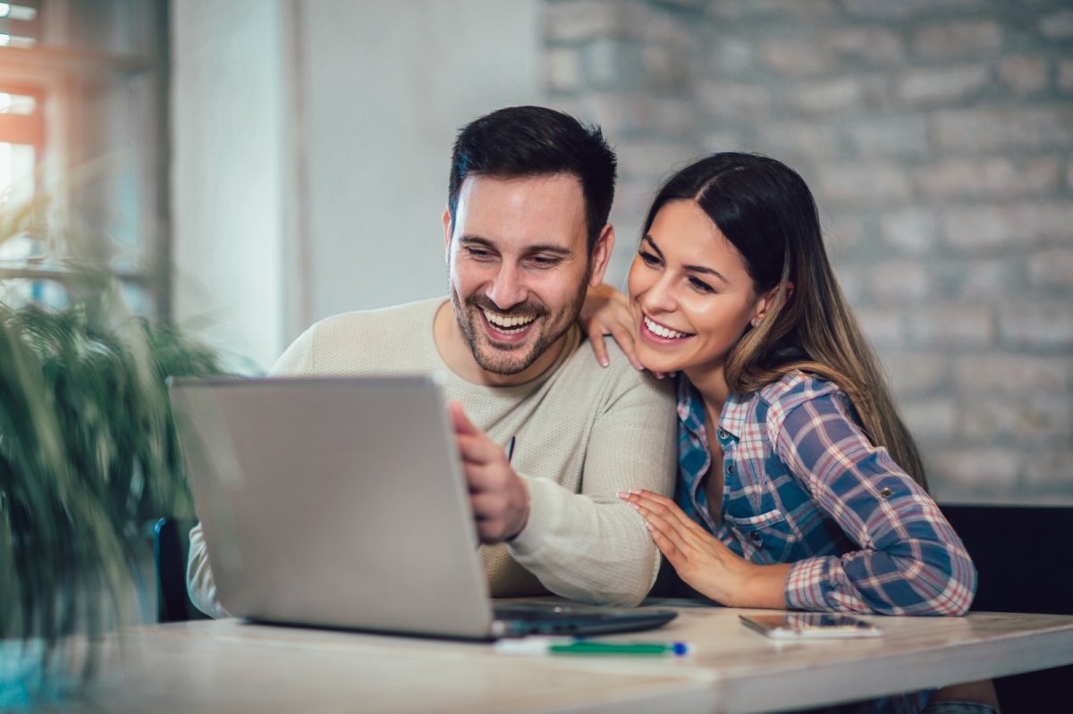 Ein Mann und eine Frau blicken glücklich auf einen Laptop.