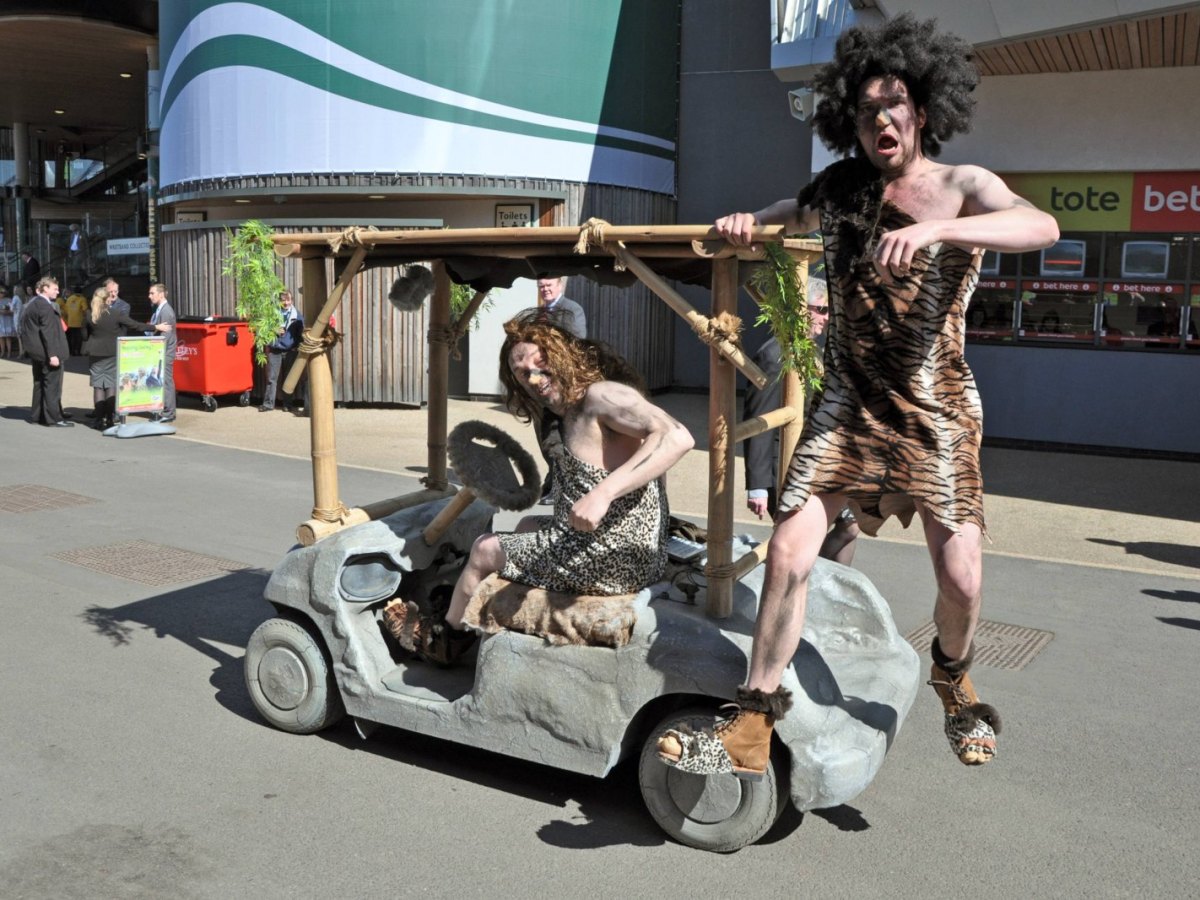 Männer als Neandertaler verkleidet fahren auf Steinzeit-Mobil.