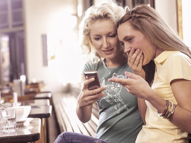 Frauen sehen peinlich berührt auf ein Smartphone