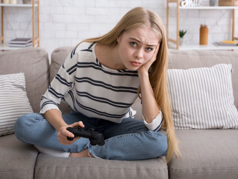 Eine junge Frau blickt mit einem Controller in der Hand skeptisch drein.