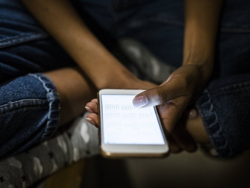 Frau im Schneidersitz hält Smartphone in der Hand