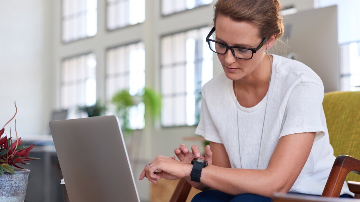 Frau mit Smartwatch vor Laptop.