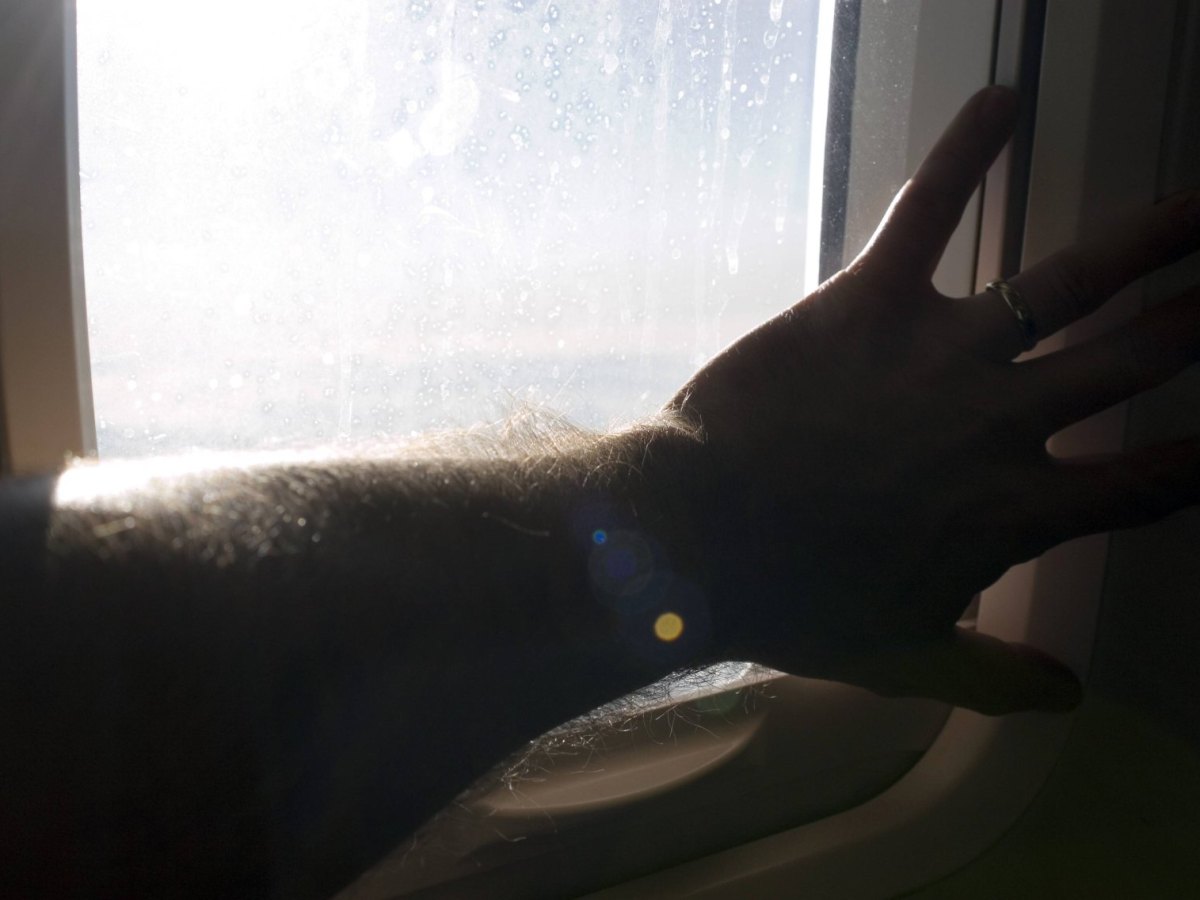 Passagier hält sich bei Turbulenzen am Flugzeugfenster fest.