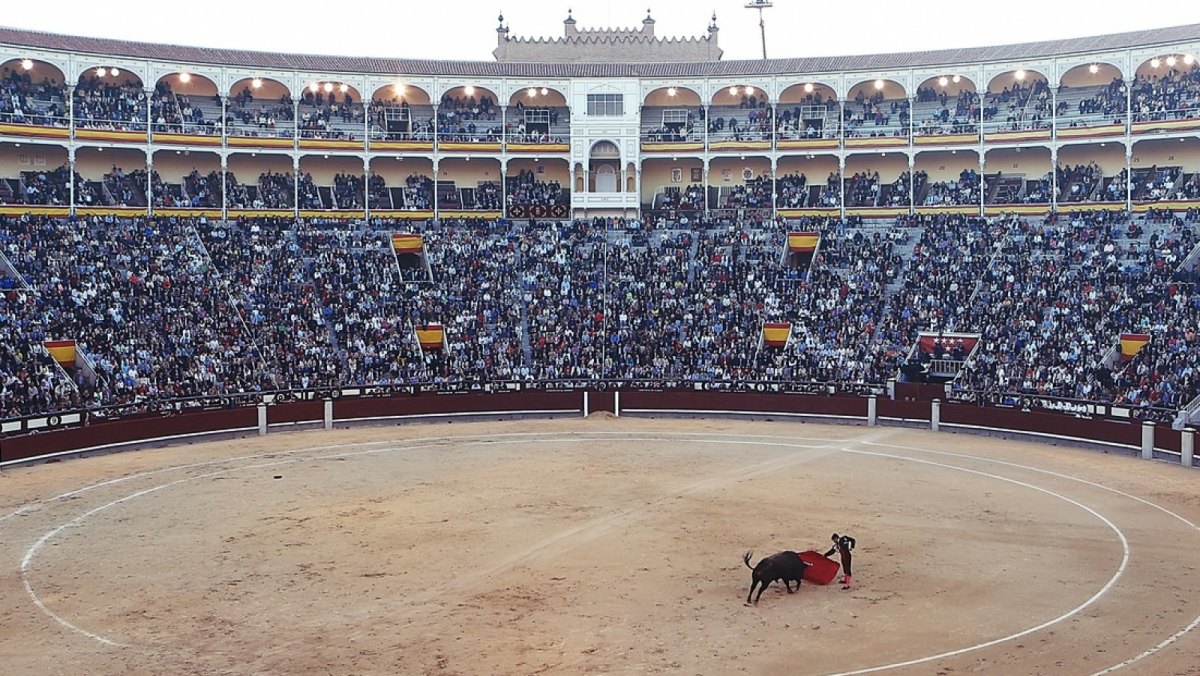 Eine Stierkampf-Arena. In der Mitte kämpfen ein Torero und ein Stier.