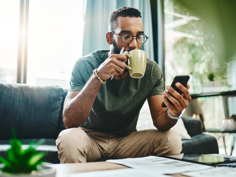 Mann trinkt Kaffee und schaut auf sein Handy.