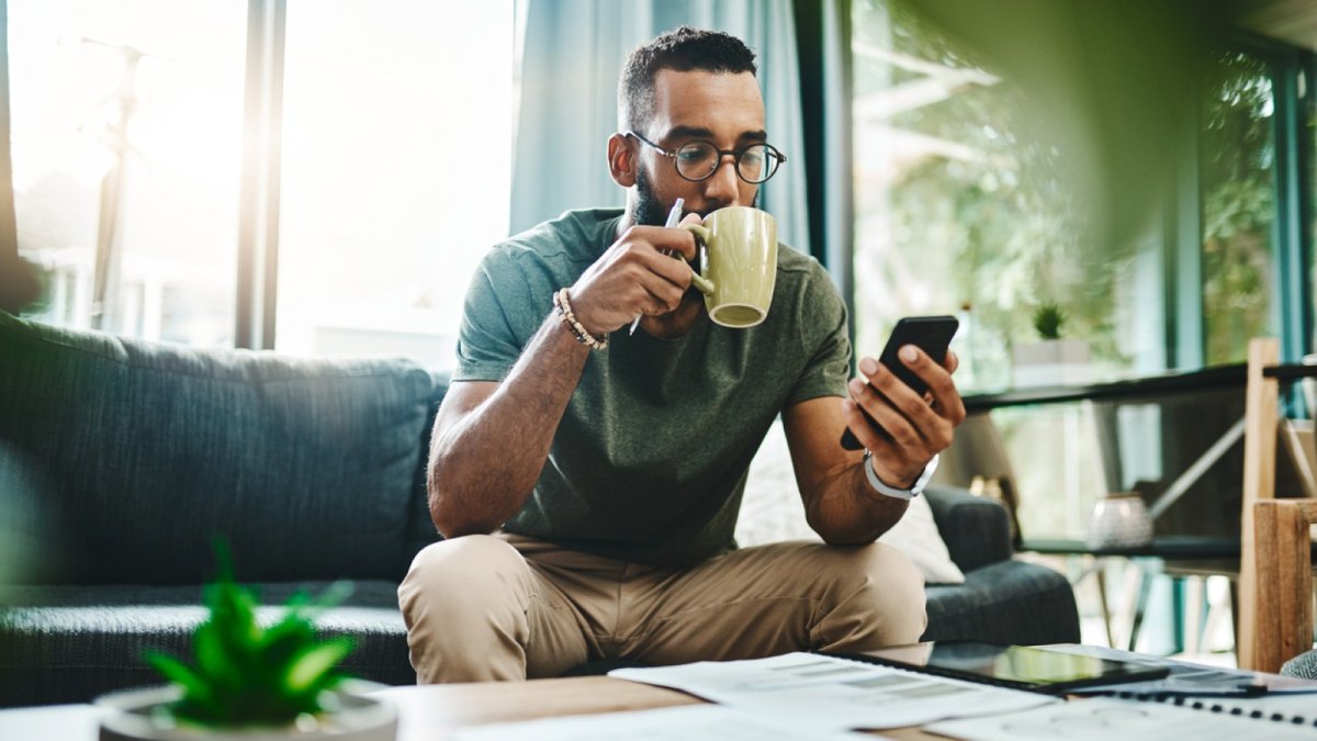 Mann trinkt Kaffee und schaut auf sein Handy.