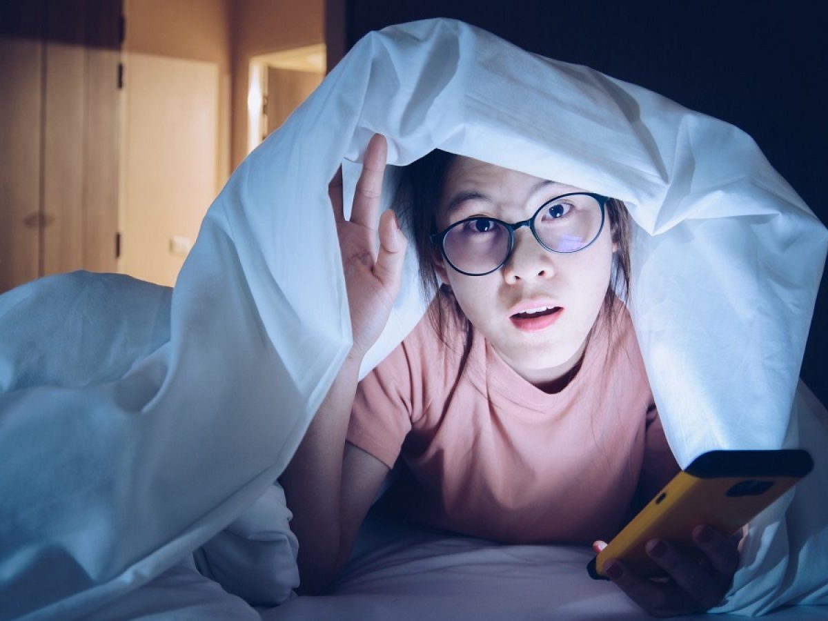 Frau mit Handy im Dunkeln unter der Decke.