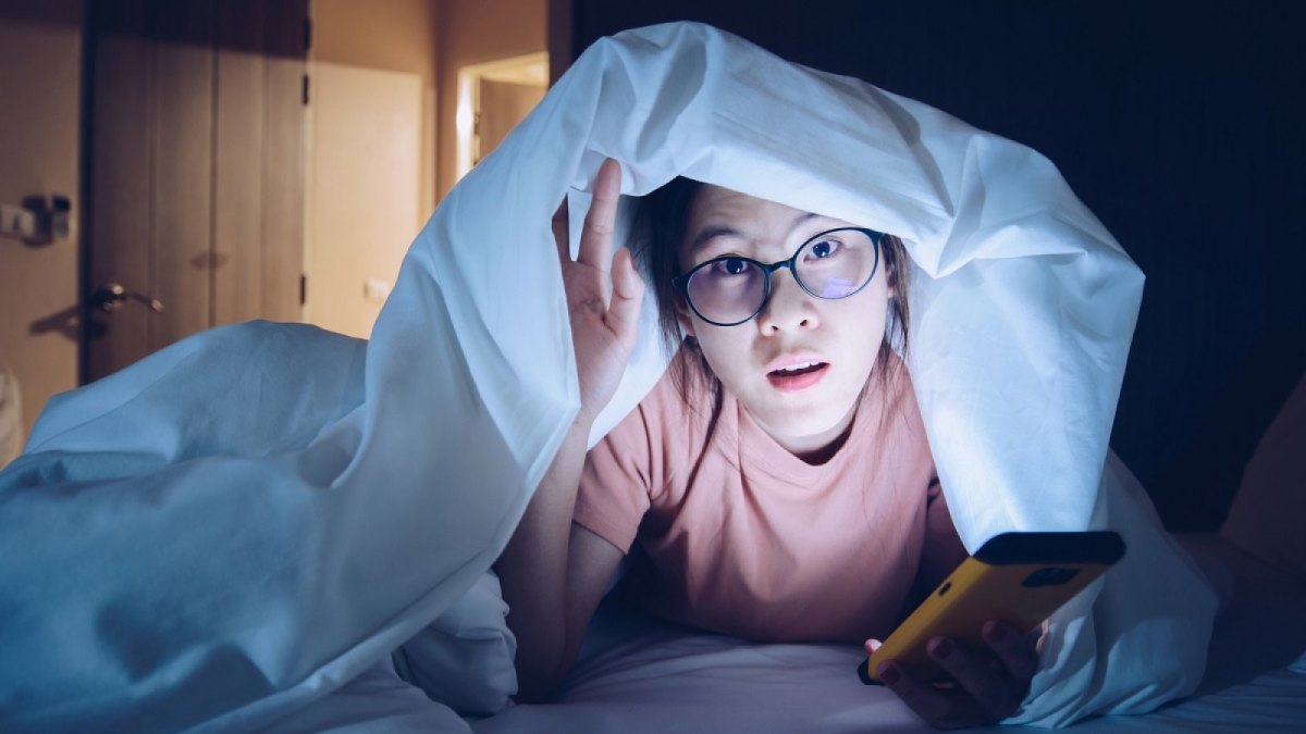 Frau mit Handy im Dunkeln unter der Decke.