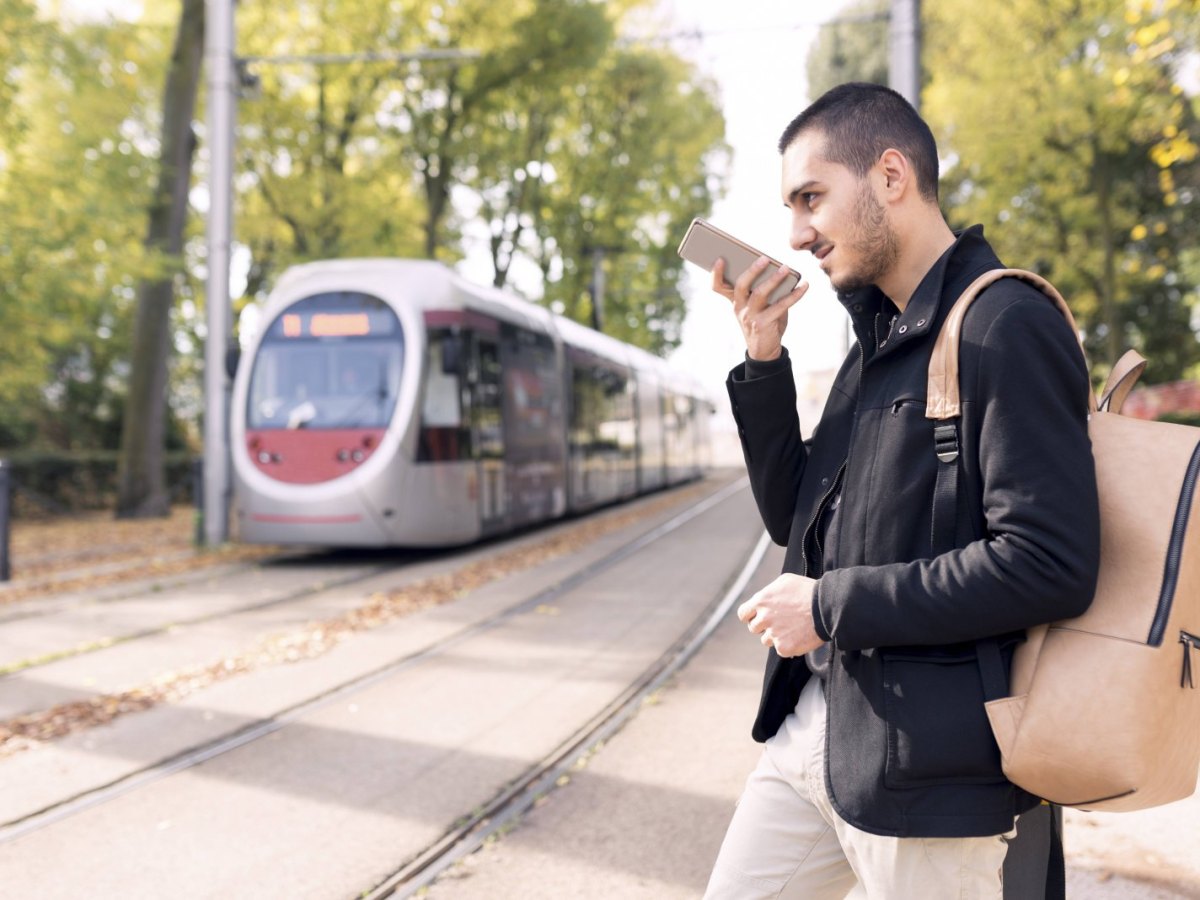 Mann spricht in Smartphone während er bei herannahendem Zug über die Gleise läuft