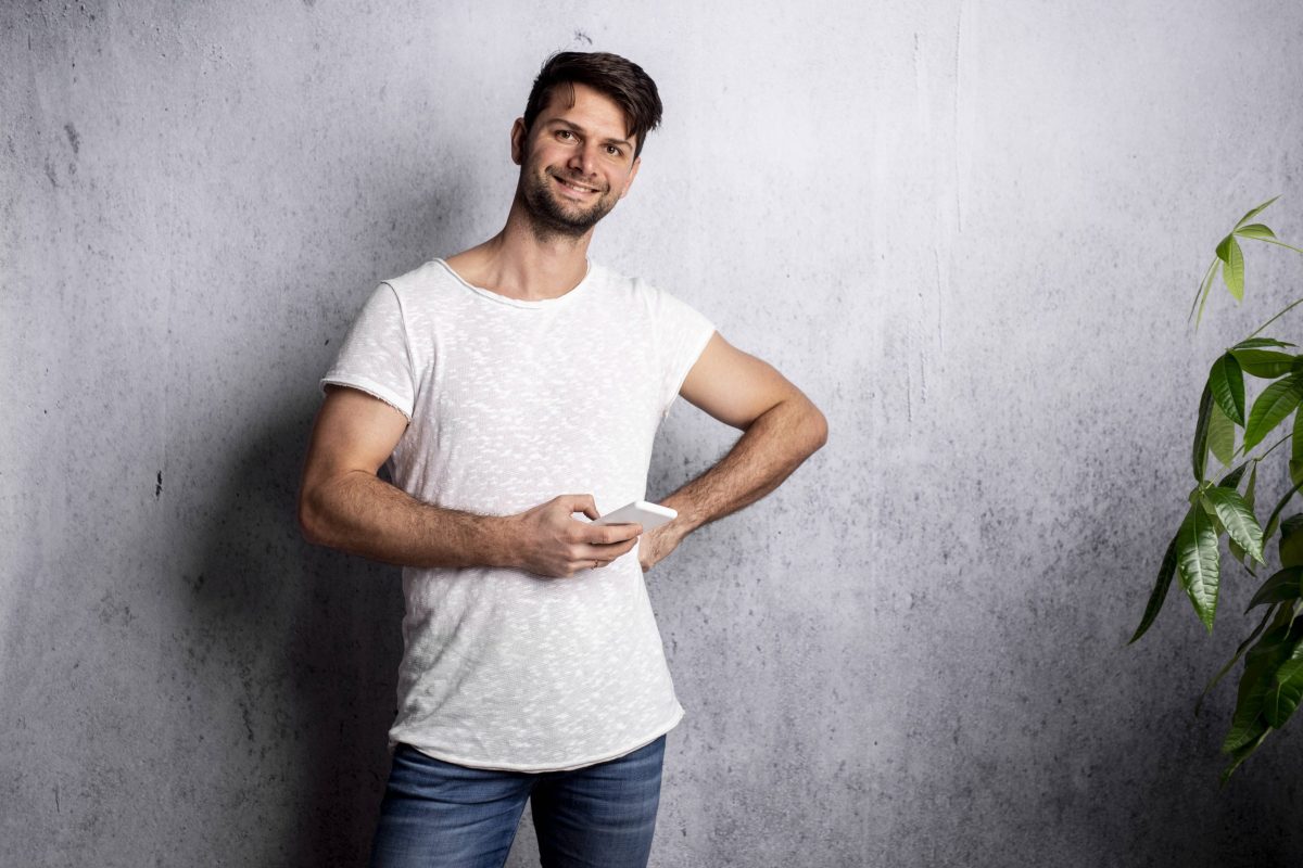 Mann steht vor Wand mit Smartphone