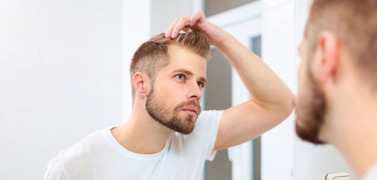 Mann begutachtet seine Haare vor dem Spiegel.