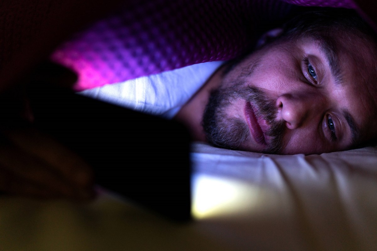Mann liegt mit Smartphone im Bett