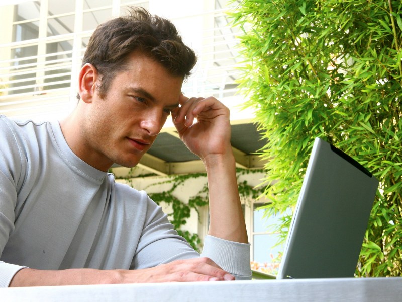 Mann sitzt vor Laptop mit fragendem Blick