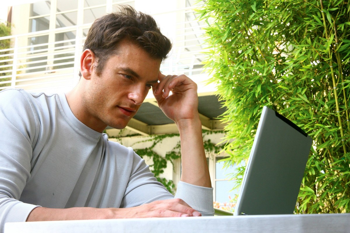 Mann sitzt vor Laptop mit fragendem Blick