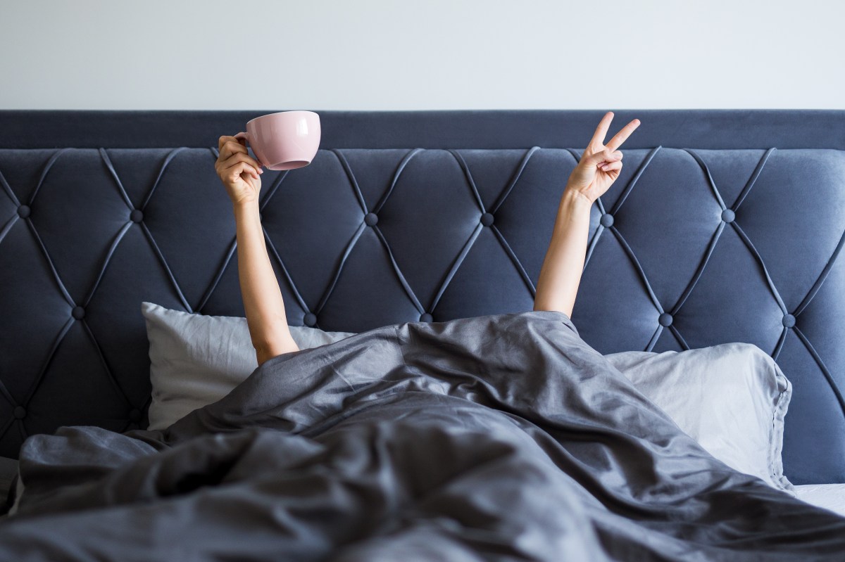 Frau im Bett hält Kaffee hoch