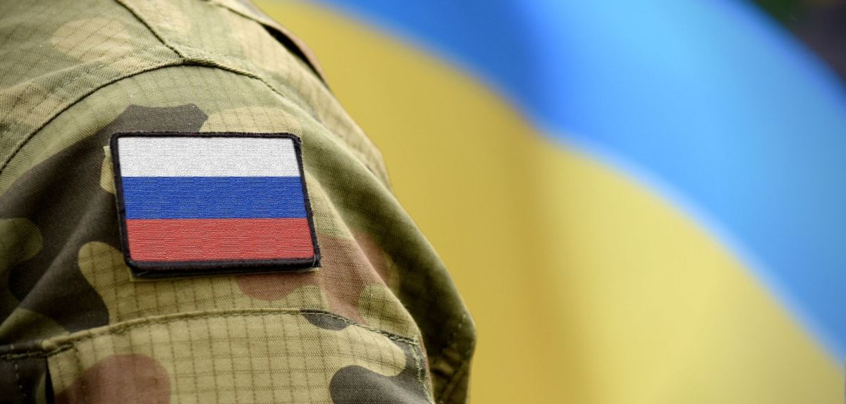 Russischer Soldat vor einer Ukraine-Flagge