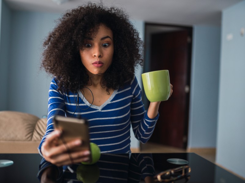 Frau mit Handy und Tasse in der Hand