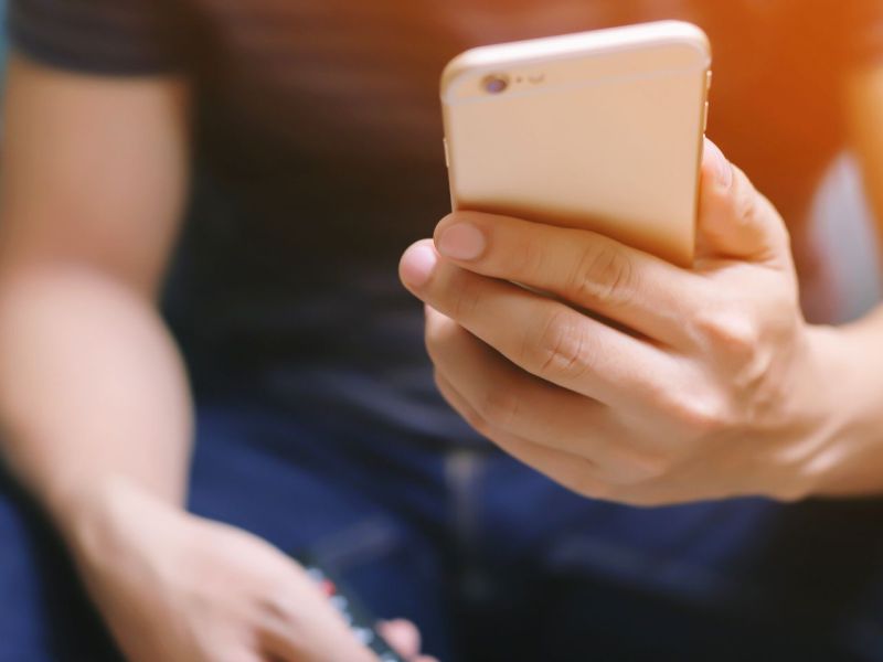 Mann mit Fernbedienung und Smartphone in der Hand