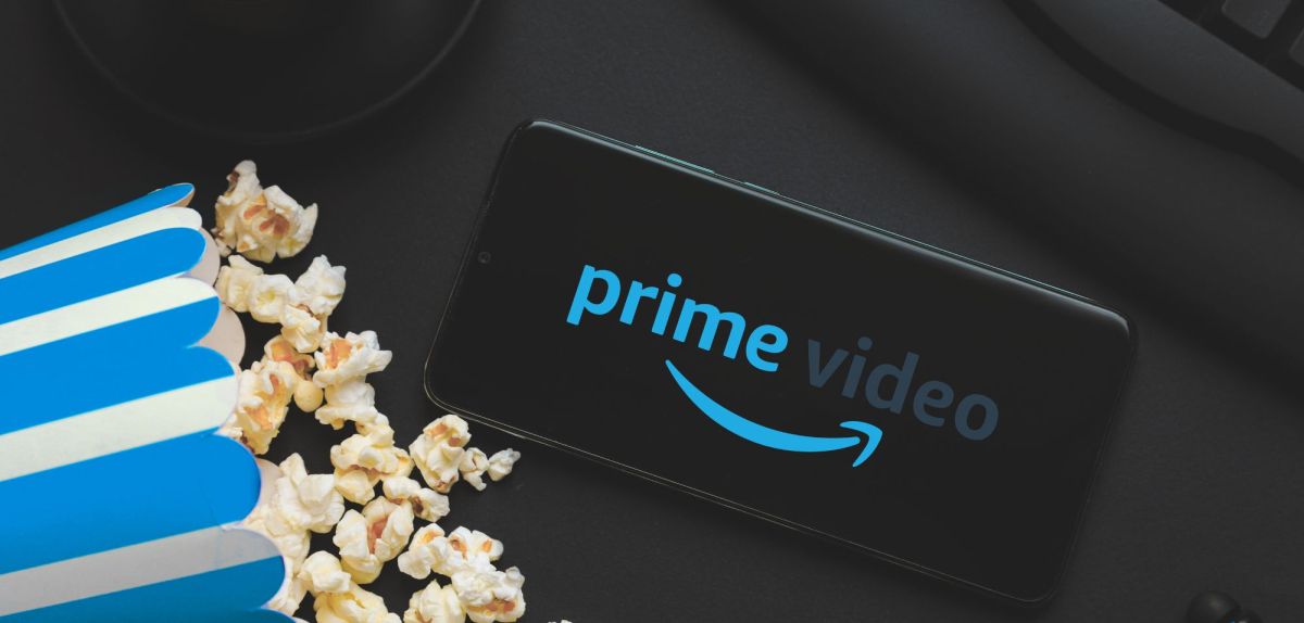 Logo von Amazon Prime Video auf einem Handy, daneben eine Tüte Popcorn.