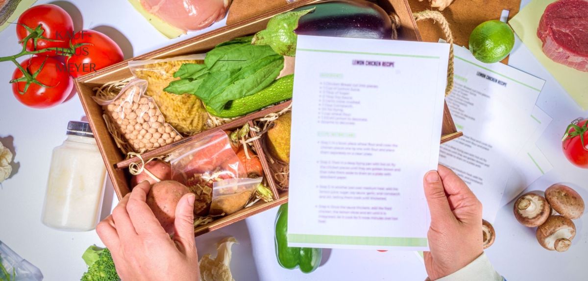 Person hält Rezept über eine Kochbox