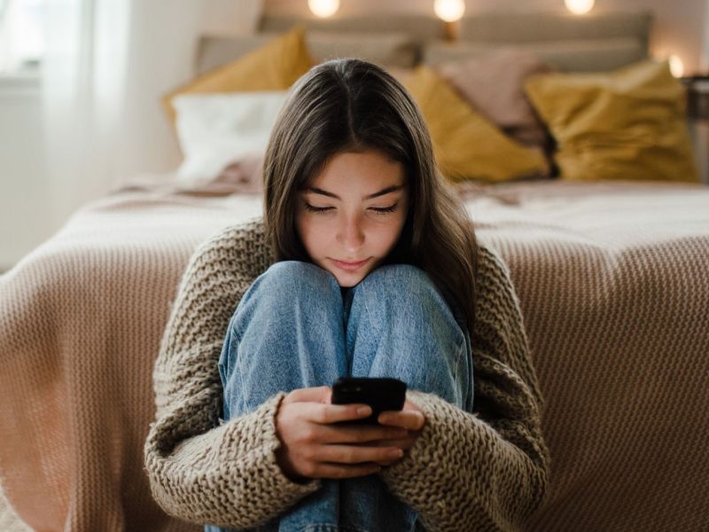 Mädchen sitzt Zuhause auf dem Boden an ihrem Handy.