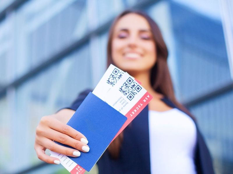 Frau hält Flugtickets in die Kamera.