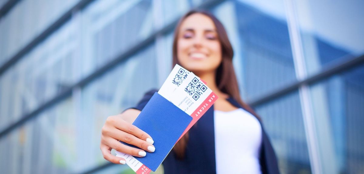 Frau hält Flugtickets in die Kamera.