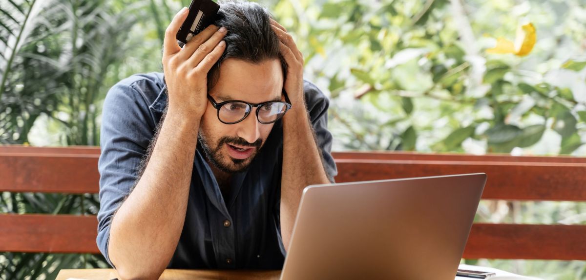 Mann schaut schockiert auf Laptop