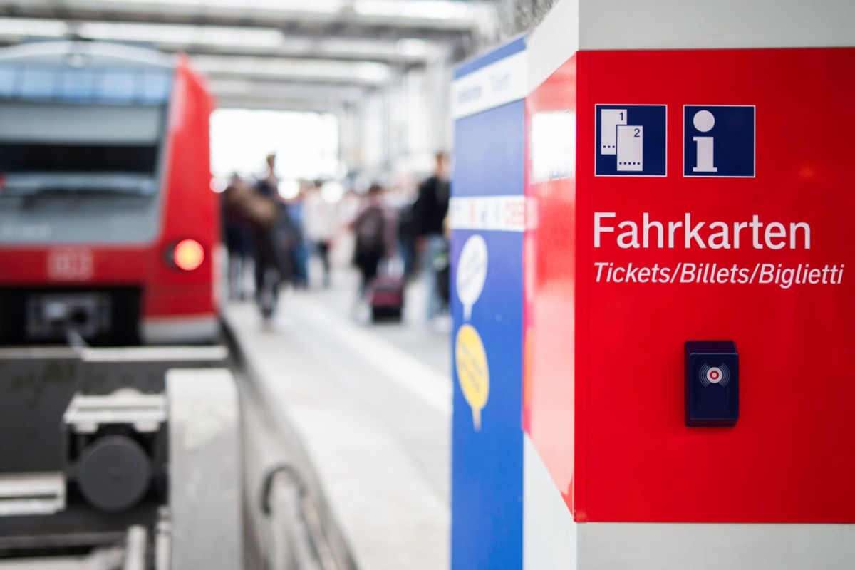 Hinweis auf Tickets am Bahnhof mit Zug im Hintergrund