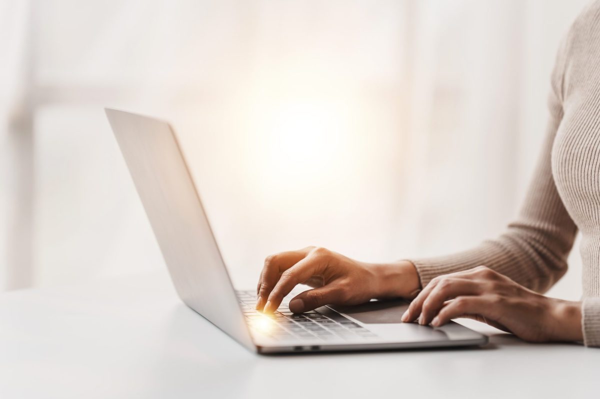 Eine Frau sitzt am Tisch und schreibt auf ihrem Laptop.