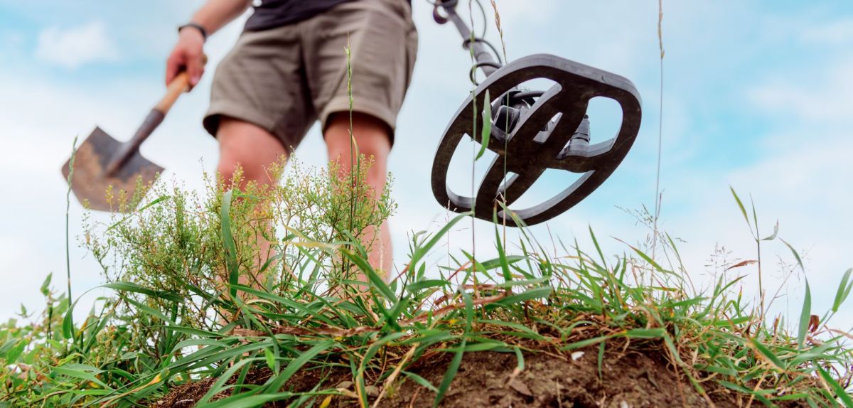 Mann mit Schaufel und Metalldetektor auf einem Feld.