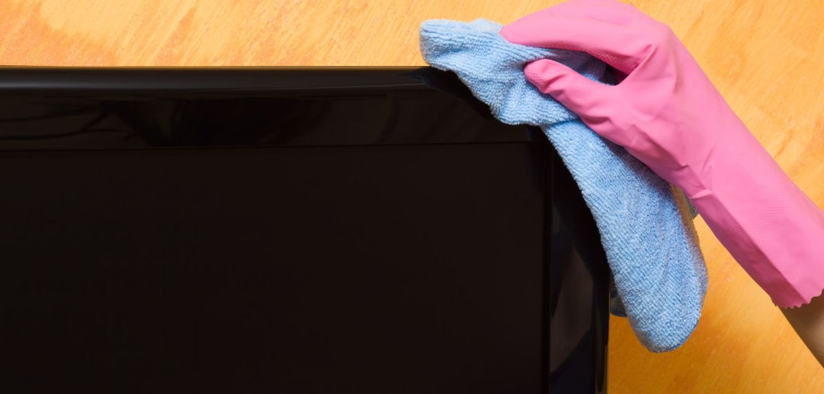 Hand mit Handschuh beim Fernseher reinigen.