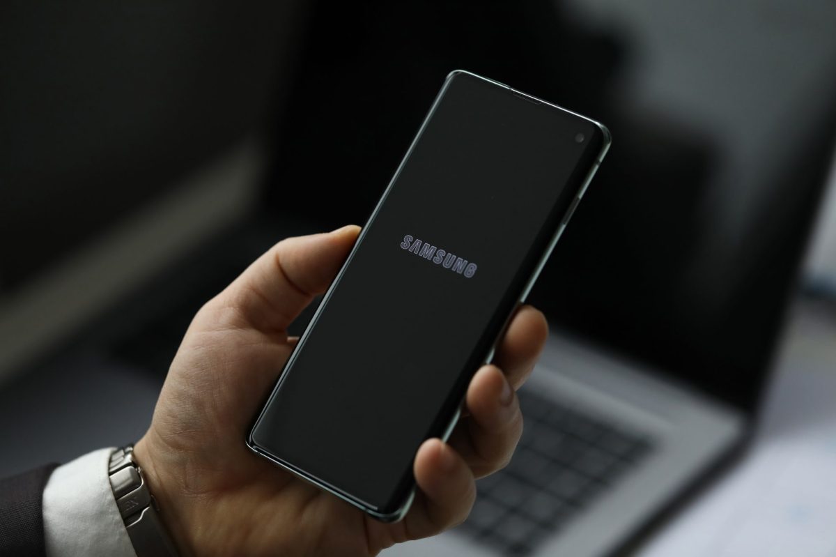 Hand hält ein Samsung Galaxy Handy über einen Laptop.