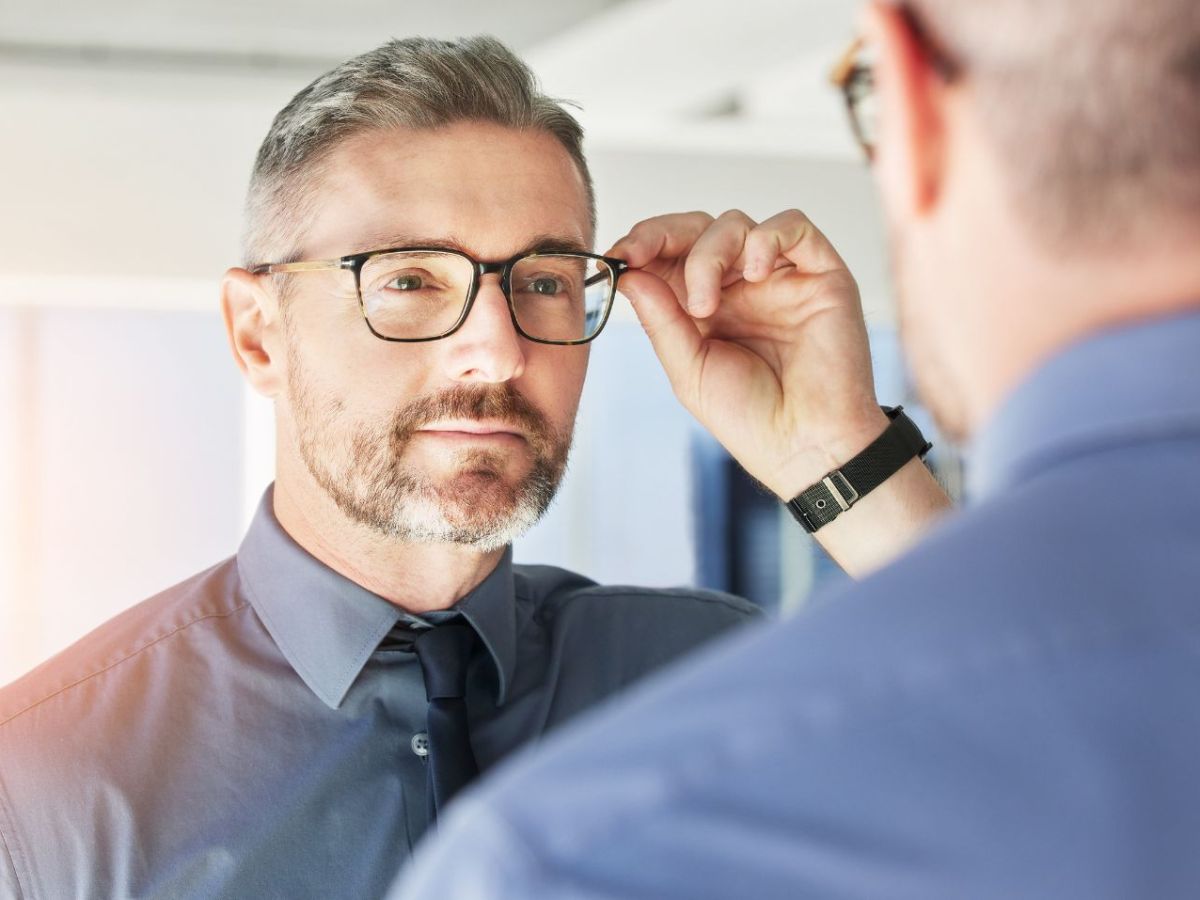 Mann schaut in den Spiegel mit Brille