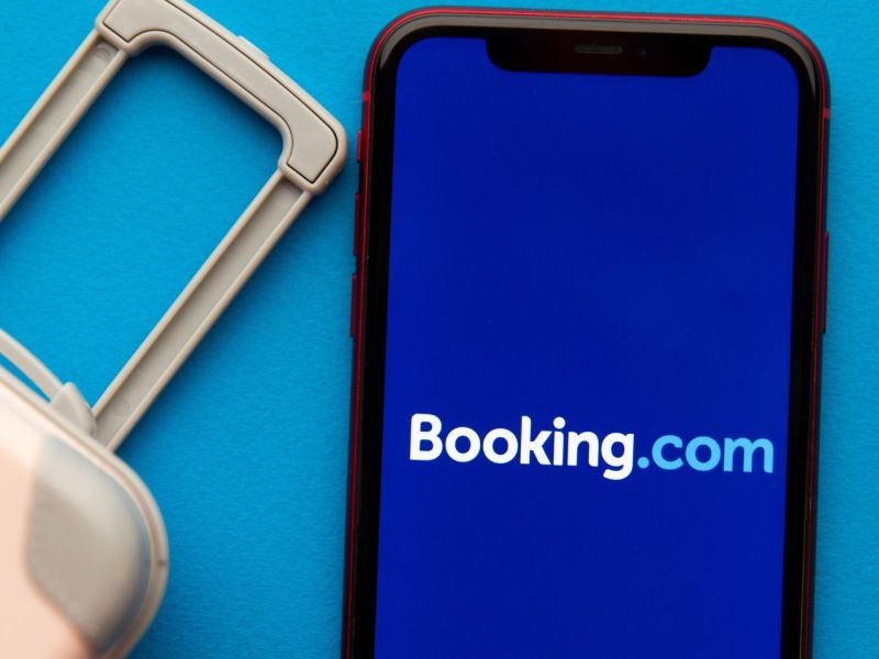 Booking.com-Schriftzug auf einem Handy, daneben ein Koffer.