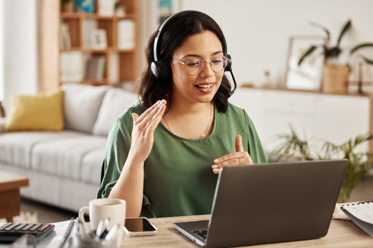 Frau sitzt vor einem Laptop und telefoniert mit Headset.