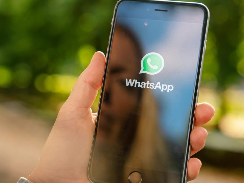 Eine blonde Frau spiegelt sich auf ihrem Smartphone während sie WhatsApp öffnet.