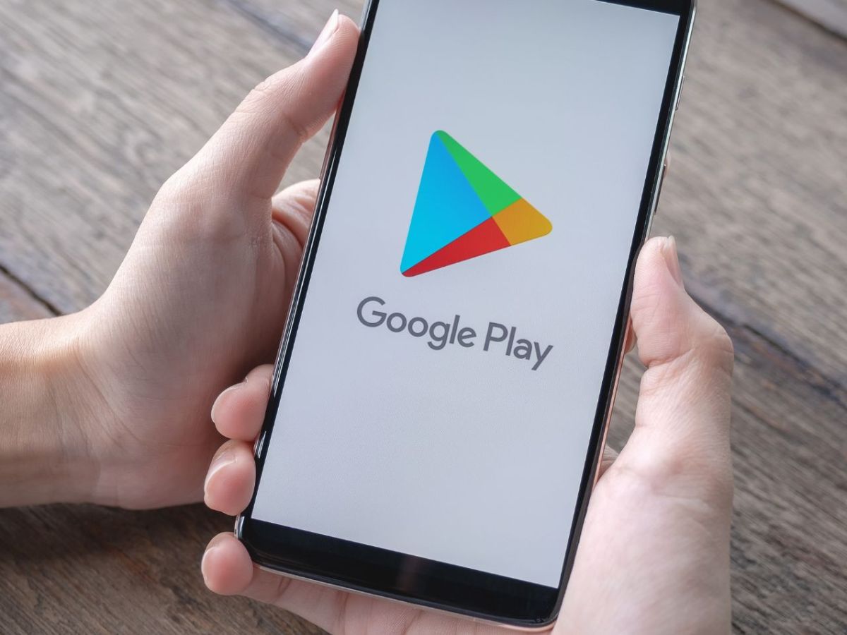 Person hält Handy mit dem Google Play Store auf dem Display in Händen.