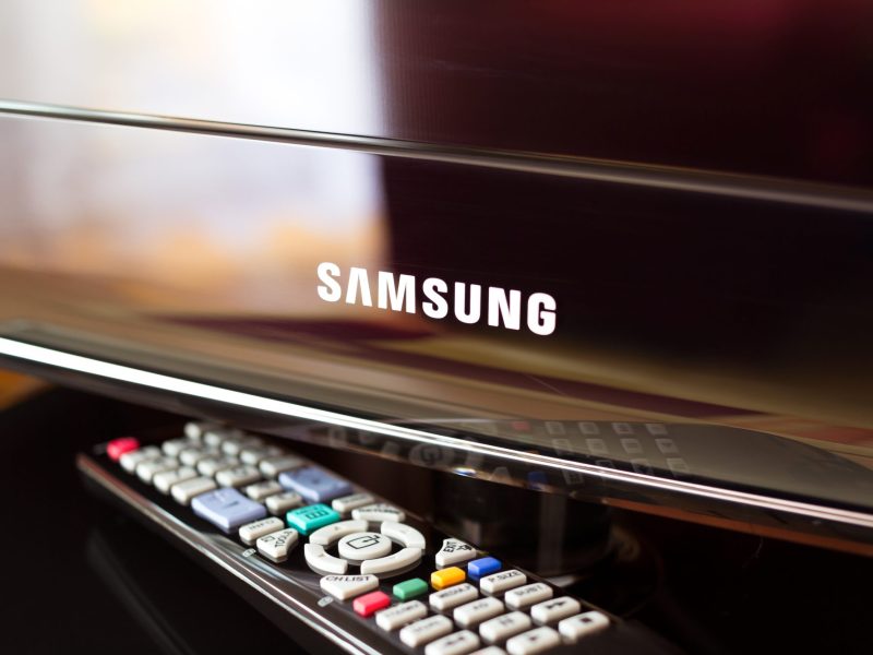 Samsung TV-Bildschirm, vor dem eine Fernbedienung liegt.