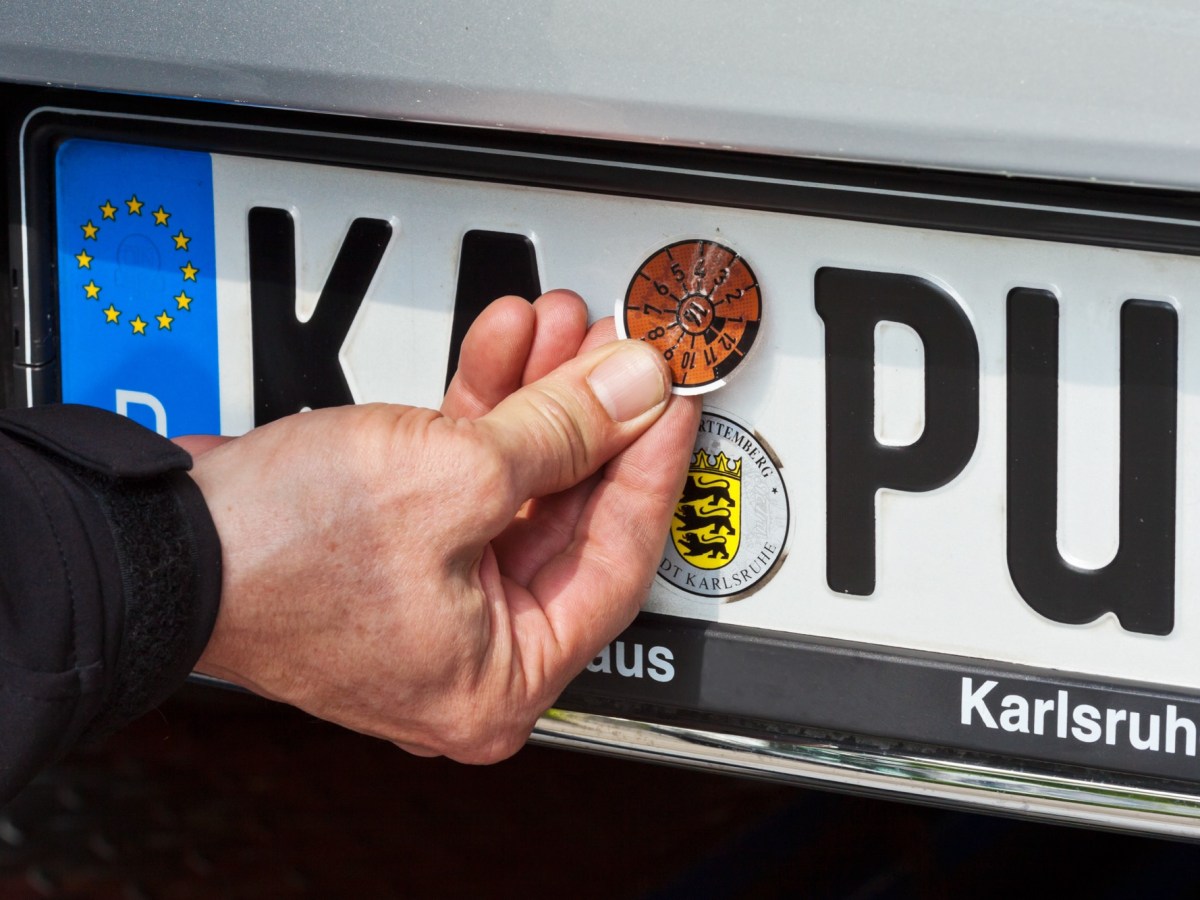 Mann klebt die HU-Plakette auf das Nummernschild