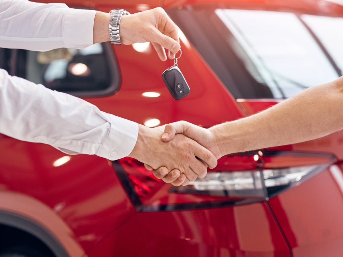 Zwei Personen geben sich die Hand, eine überreicht einen Autoschlüssel