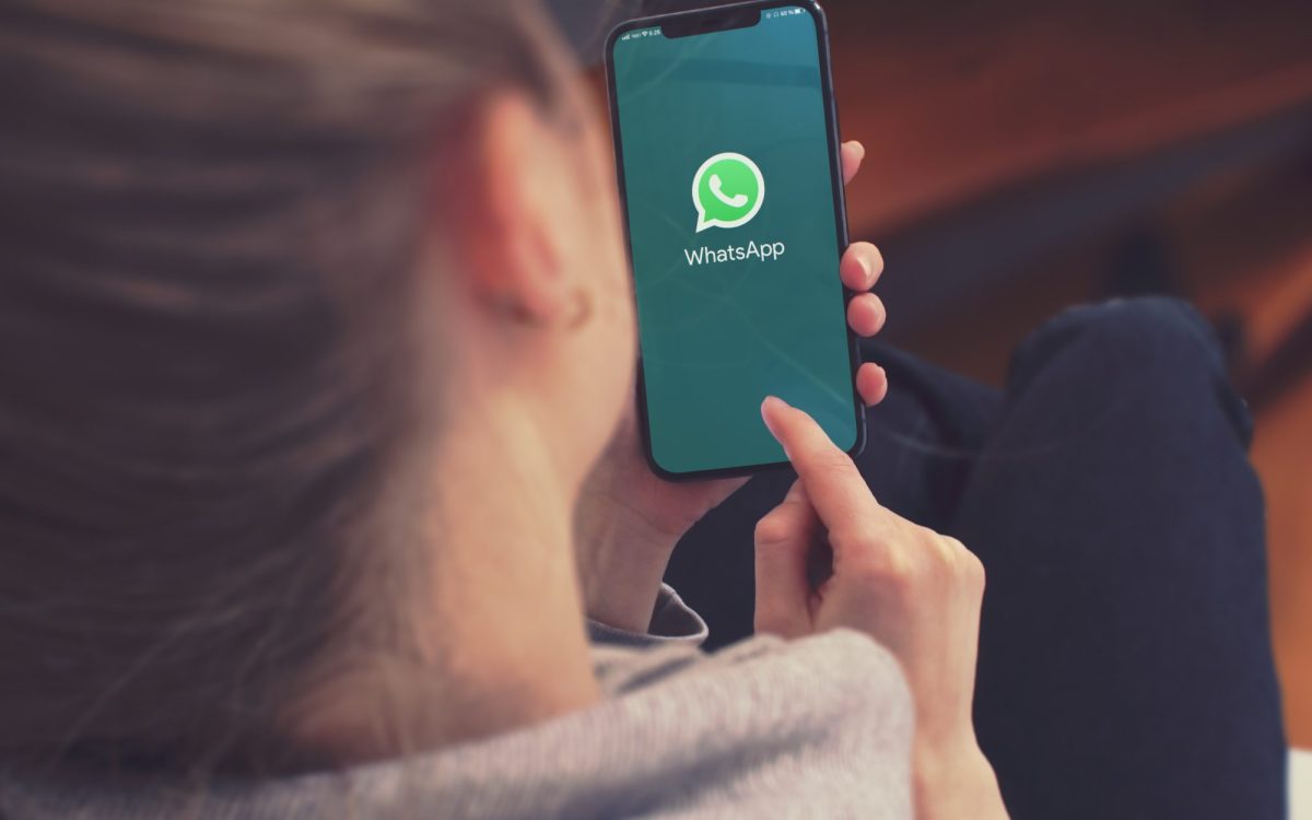 Eine Frau hält ein Handy in der Hand. Auf dem Display ist das WhatsApp-Logo zu sehen.