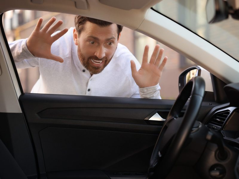 Ein blickt erschrocken durch die Scheibe eines Autos. Im Innenraum steckt der Autoschlüssel.