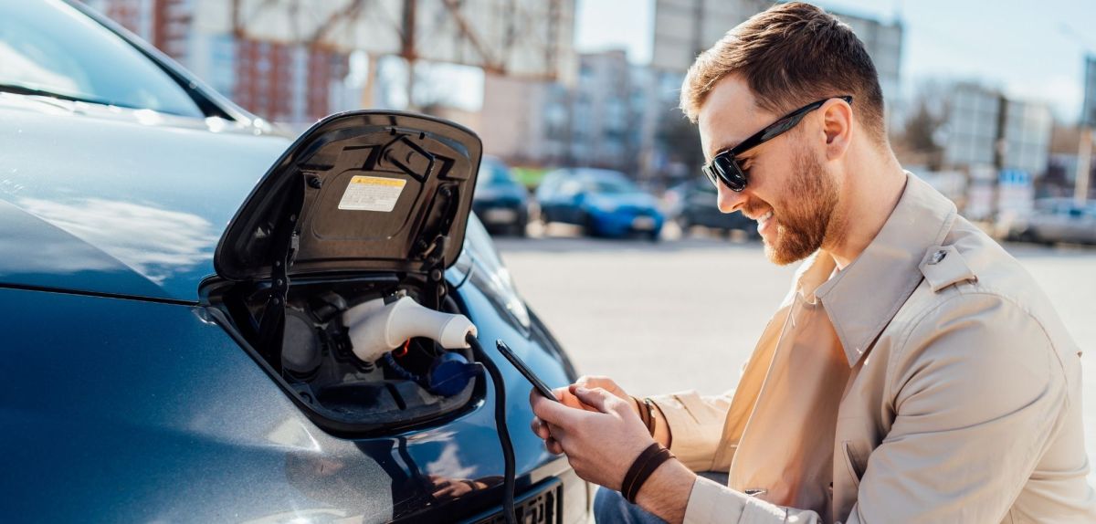 Elektroauto-Fahrer nutzt Apps auf dem Smartphone.