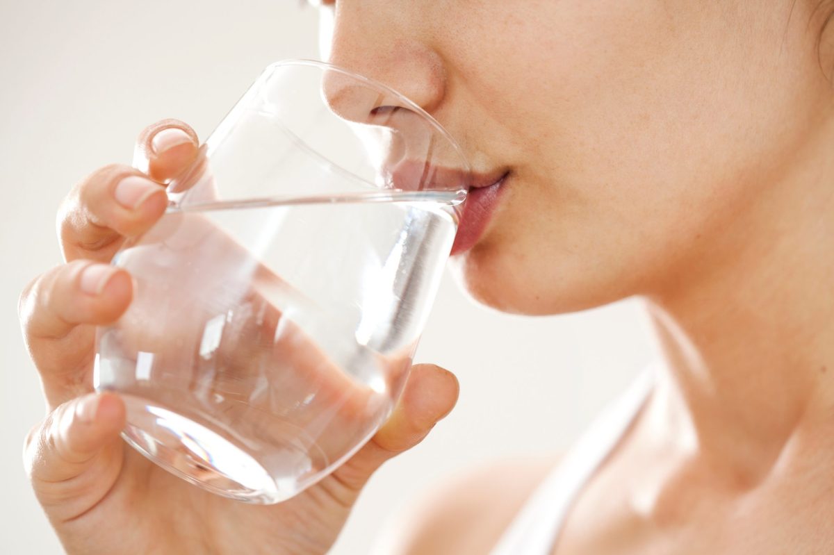 Nahaufnahme auf eine Person, die aus einem Glas Wasser trinkt.