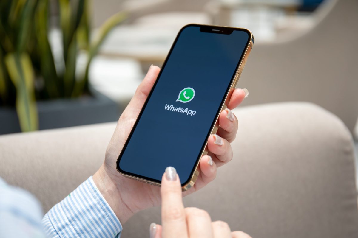 Eine Frau hält ein Smartphone in der Hand, auf dessen Display das WhatsApp-Logo angezeigt wird.