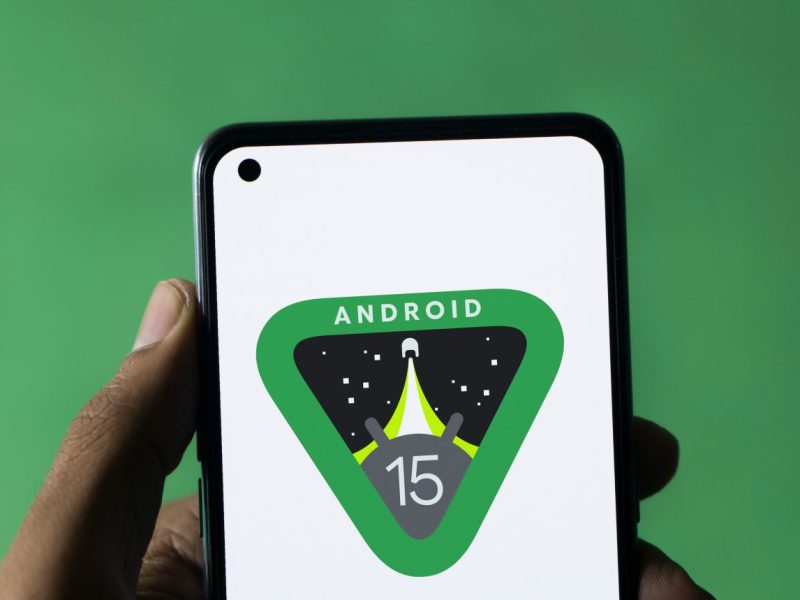 Hand hält Smartphone in der Hand, auf dem Bildschirm ist das Android 15-Logo zu sehen.