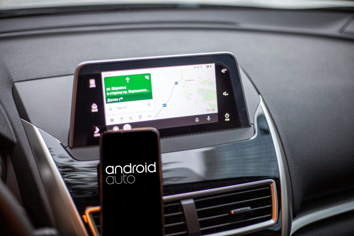 Android Auto auf einem Handy-Display. Im Hintergrund ist das Armaturenbrett eines Autos zu sehen.