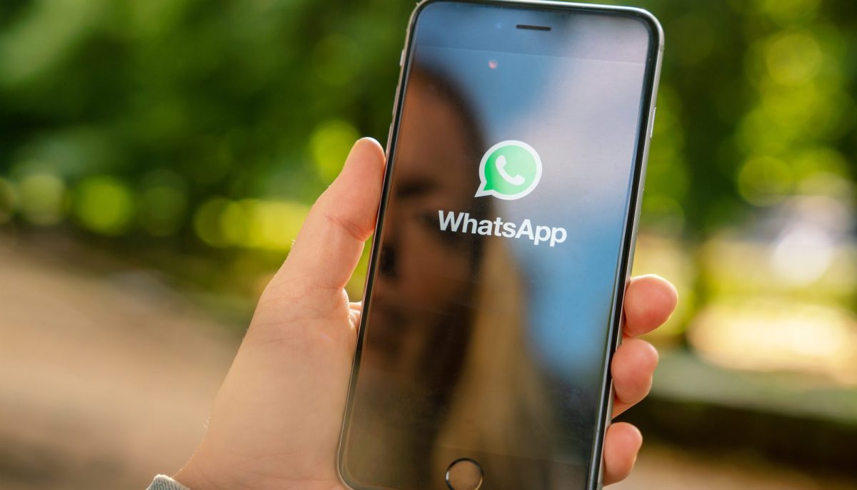 Eine Person hält ein Handy. Auf dessen Display wird das WhatsApp-Logo angezeigt.