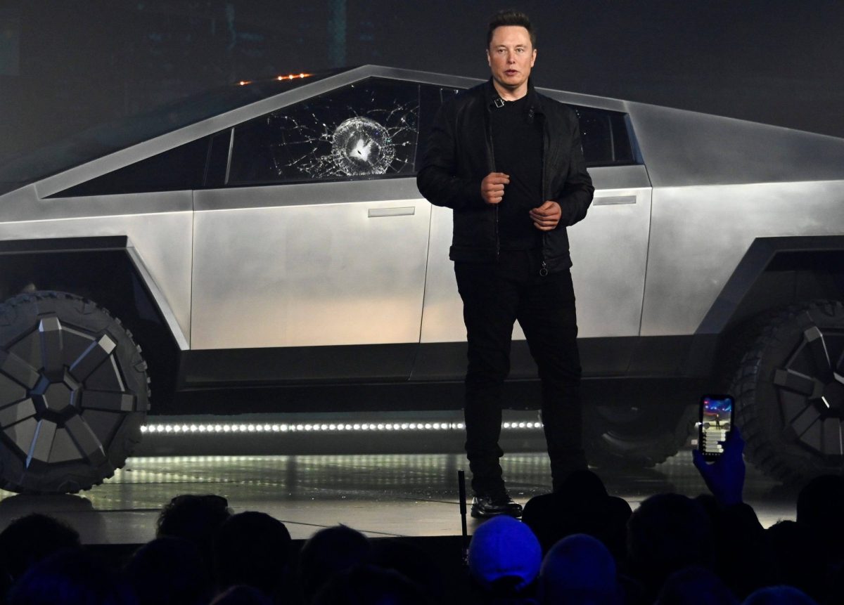 Elon Musk bei der Vorstellung des Tesla Cybertrucks 2019. Im Hintergrund ist das Fahrzeug mit kaputter Scheibe zu sehen.